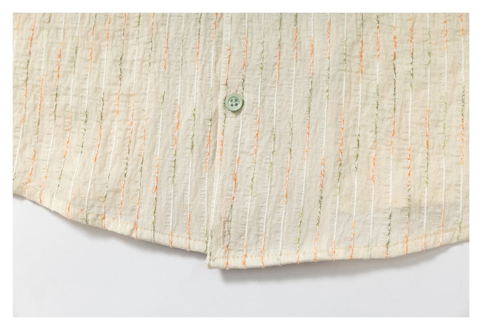 Close-up of the curved hem and button placket of an ivory shirt with fine orange and olive stripes.