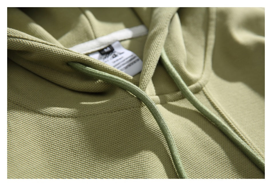 Close-up of a muted olive hoodie’s hood, matching drawstrings, and partially visible inner neck label.