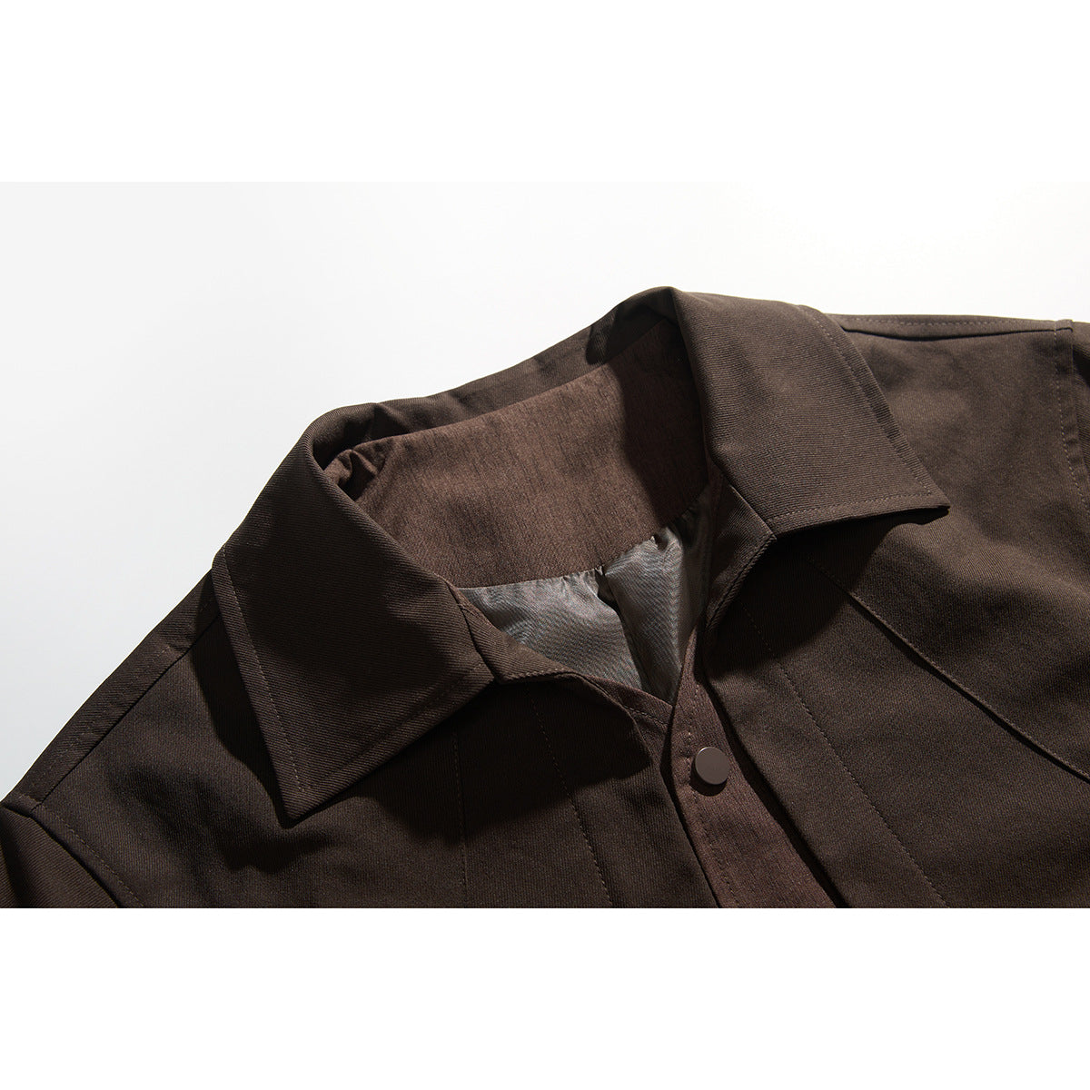 Close-up of a dark brown jacket's wide collar, inner lining, seam details and snap-button front.