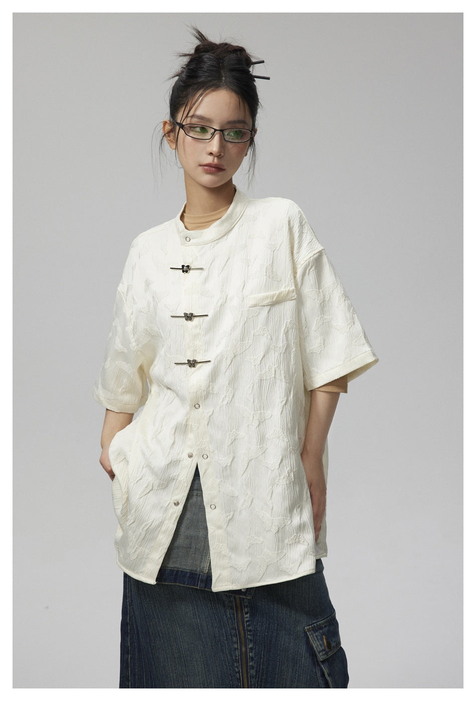 Closer front view of an ivory short-sleeve jacket with a raised pattern, stand collar, and frog closures.