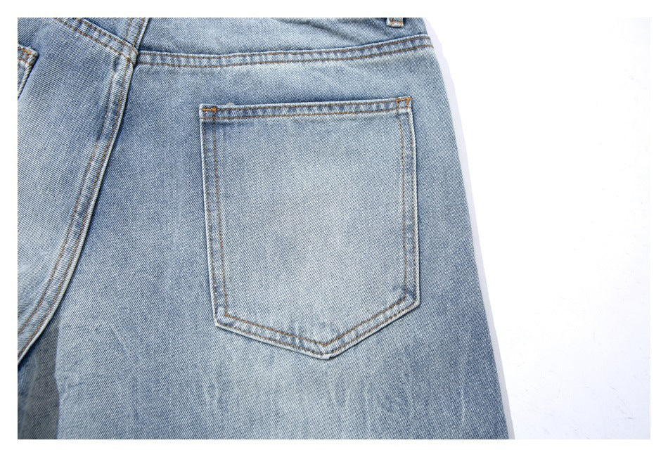 Close-up of a rear patch pocket with contrast stitching on light-wash denim shorts.