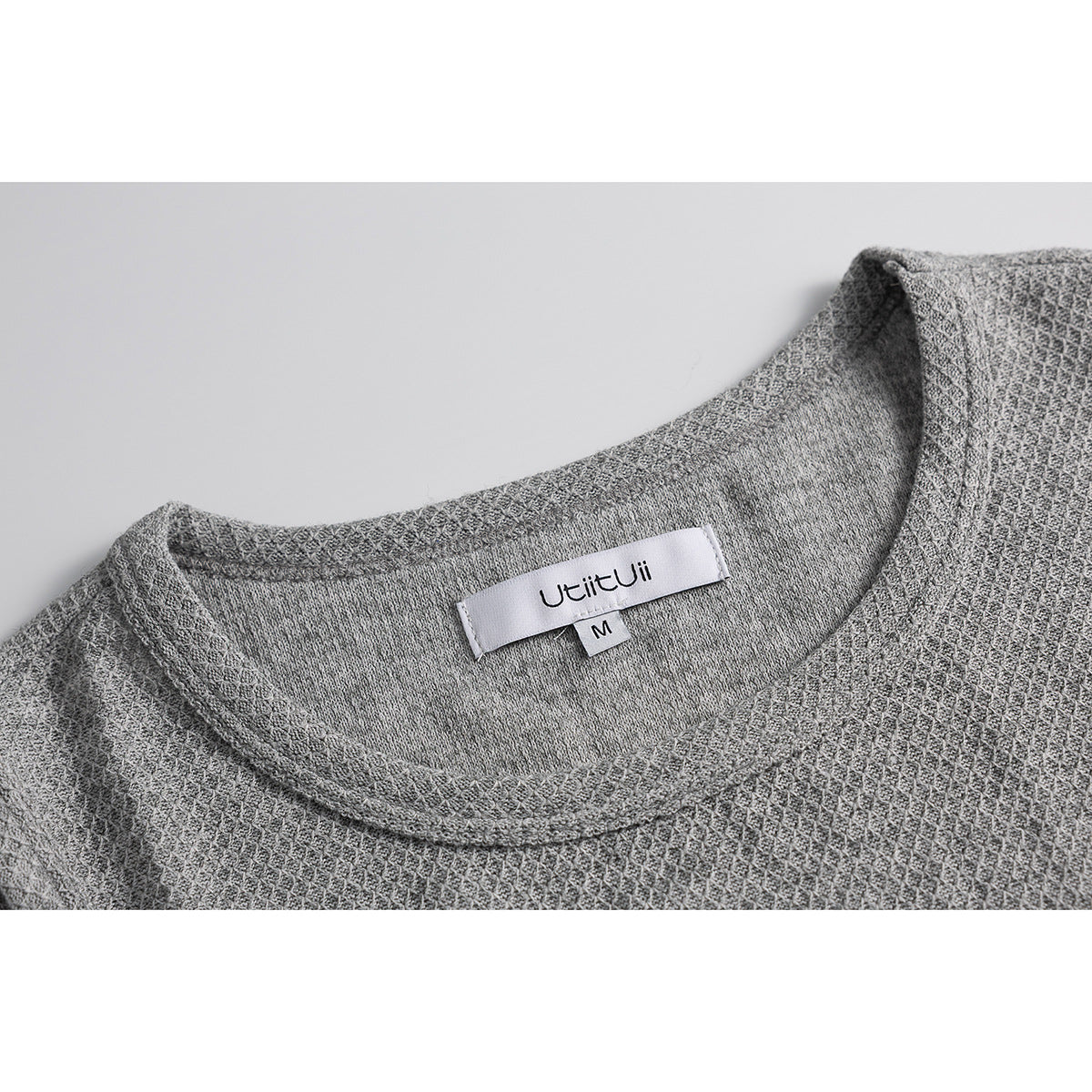 Close-up of a gray textured knit crew neckline with a sewn label marked size M.