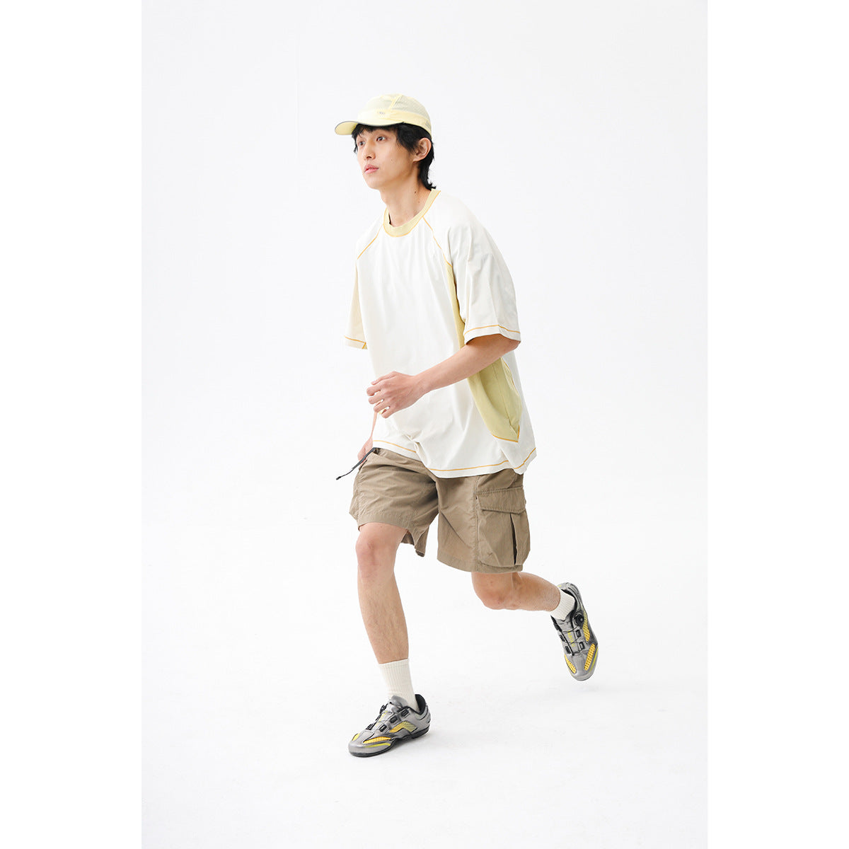 Model wearing an ivory short-sleeve shirt with yellow piping and tan cargo shorts, shown against a white studio background.