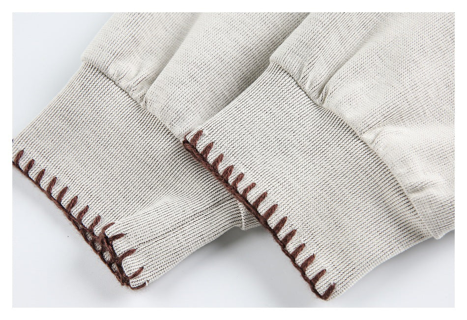 Close-up of cream sleeves with wide cuffs and brown blanket stitching along the edges.