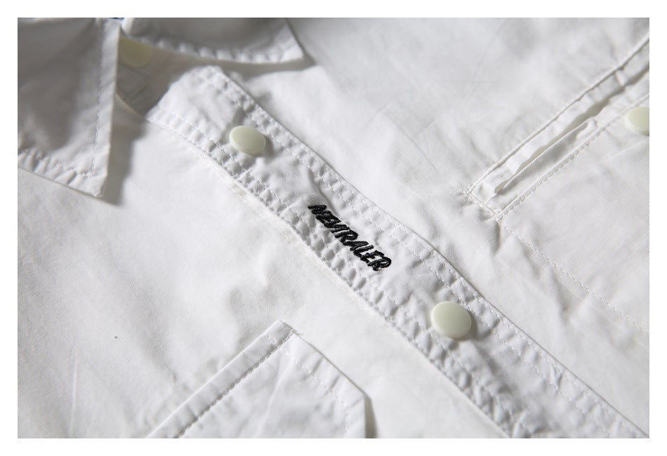 Close-up of the white shirt's placket with snap buttons, black embroidery, and a chest pocket edge.