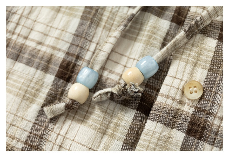 Close-up of a beige and brown plaid garment with blue and cream beads on a fabric tie and a tan button.
