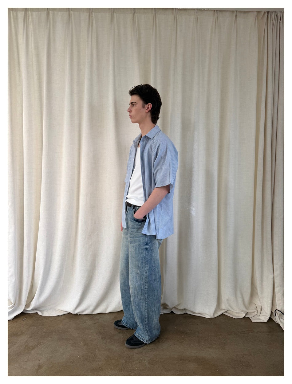 Side view of a model wearing an open blue striped short-sleeve shirt over a white top with loose blue jeans.