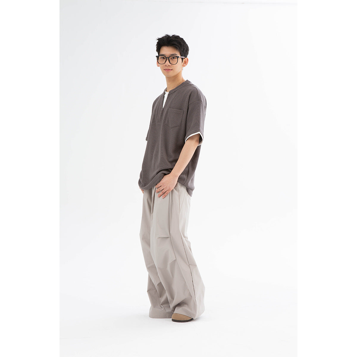 Model wearing a charcoal short-sleeve pocket shirt and loose light-gray wide-leg pants.