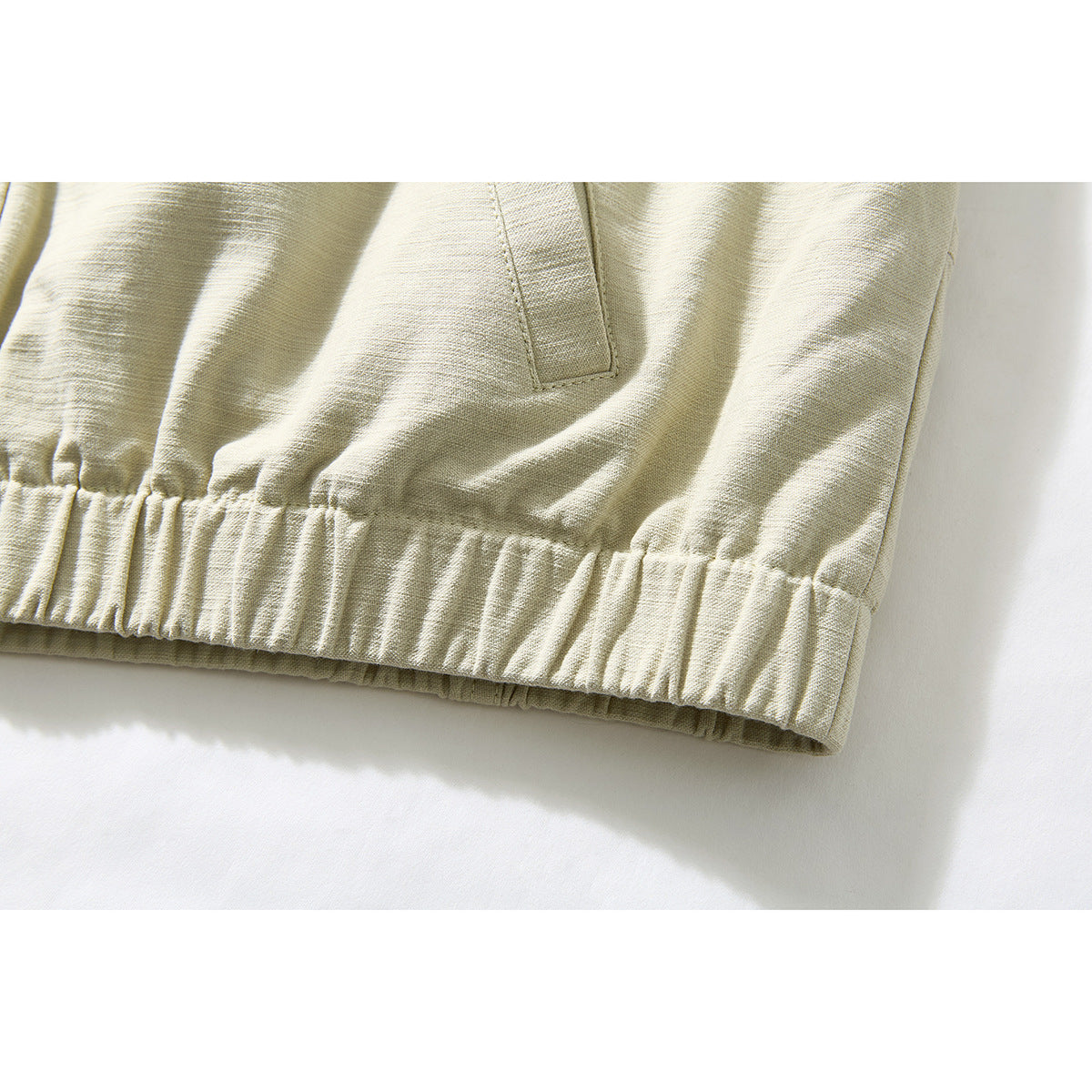 Close-up of the pale beige jacket's gathered elastic hem and lower pocket opening.