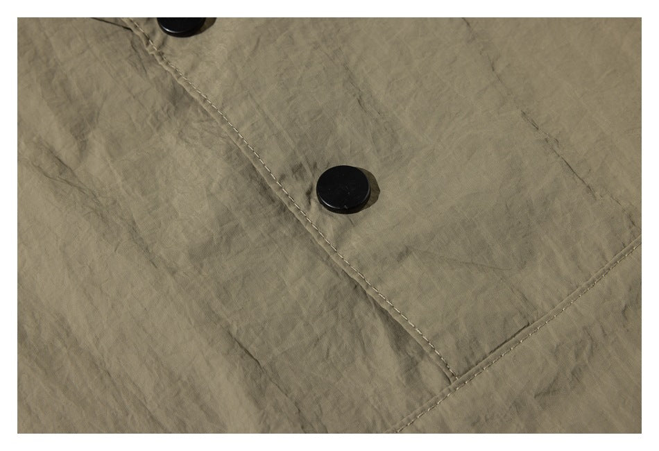 Close-up of a black snap button and stitched seam on wrinkled khaki fabric.