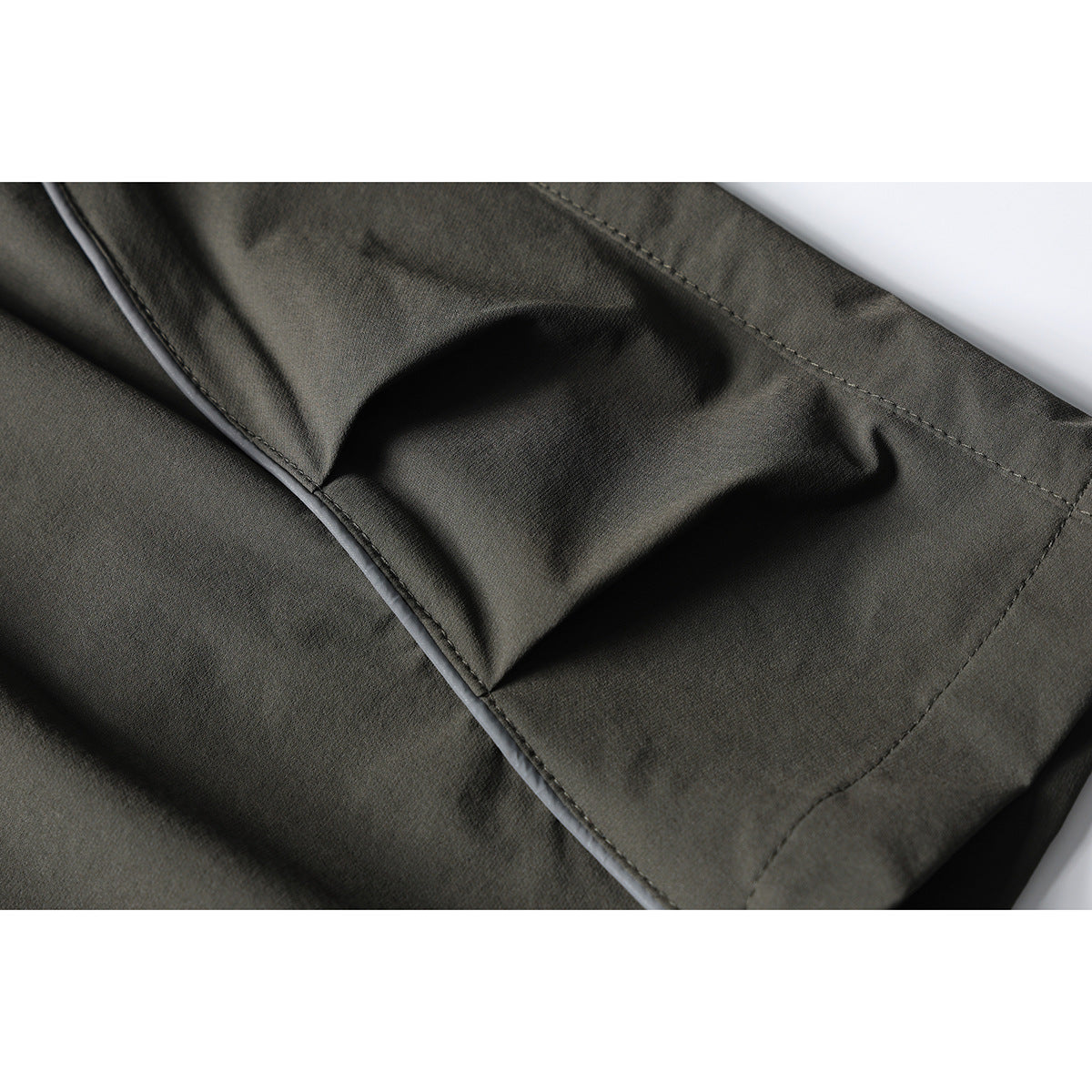 Close-up of dark olive pants showing a stitched pocket edge and fabric seams.