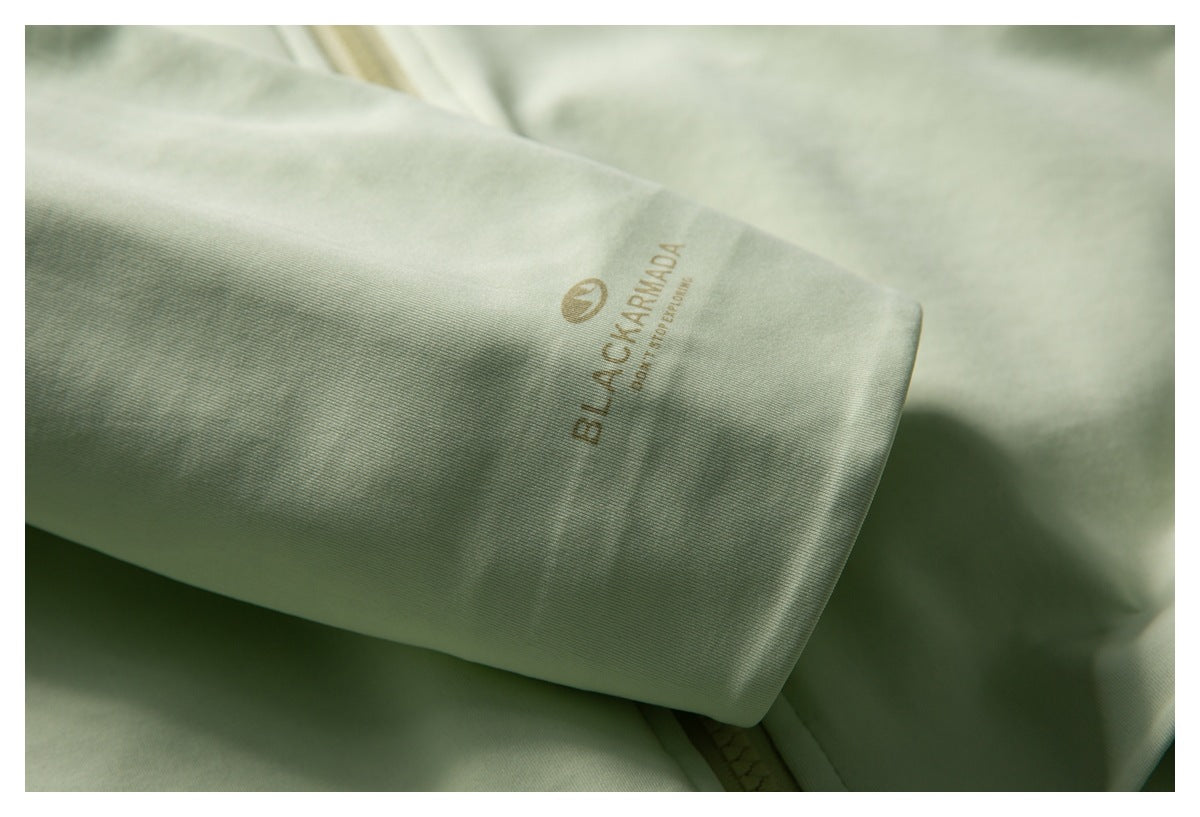 Close-up of a pale sage-green jacket sleeve cuff with a small tan Black Armada logo.