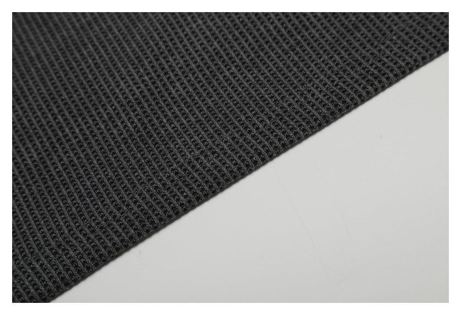 Close-up of the edge and repeating texture of dark charcoal fabric against a pale background.