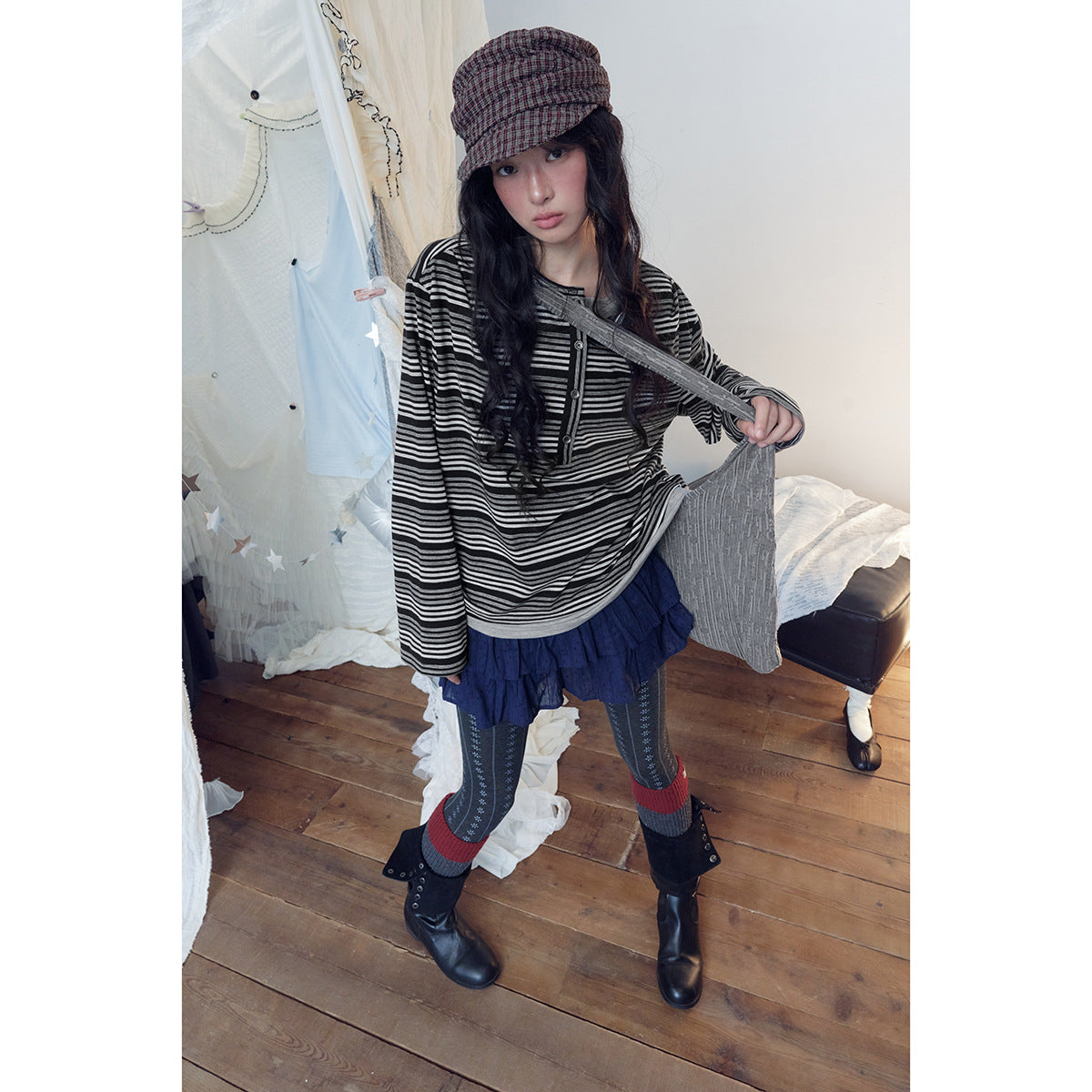 Model wearing a black and gray striped long-sleeve henley with a navy ruffled skirt and patterned tights.