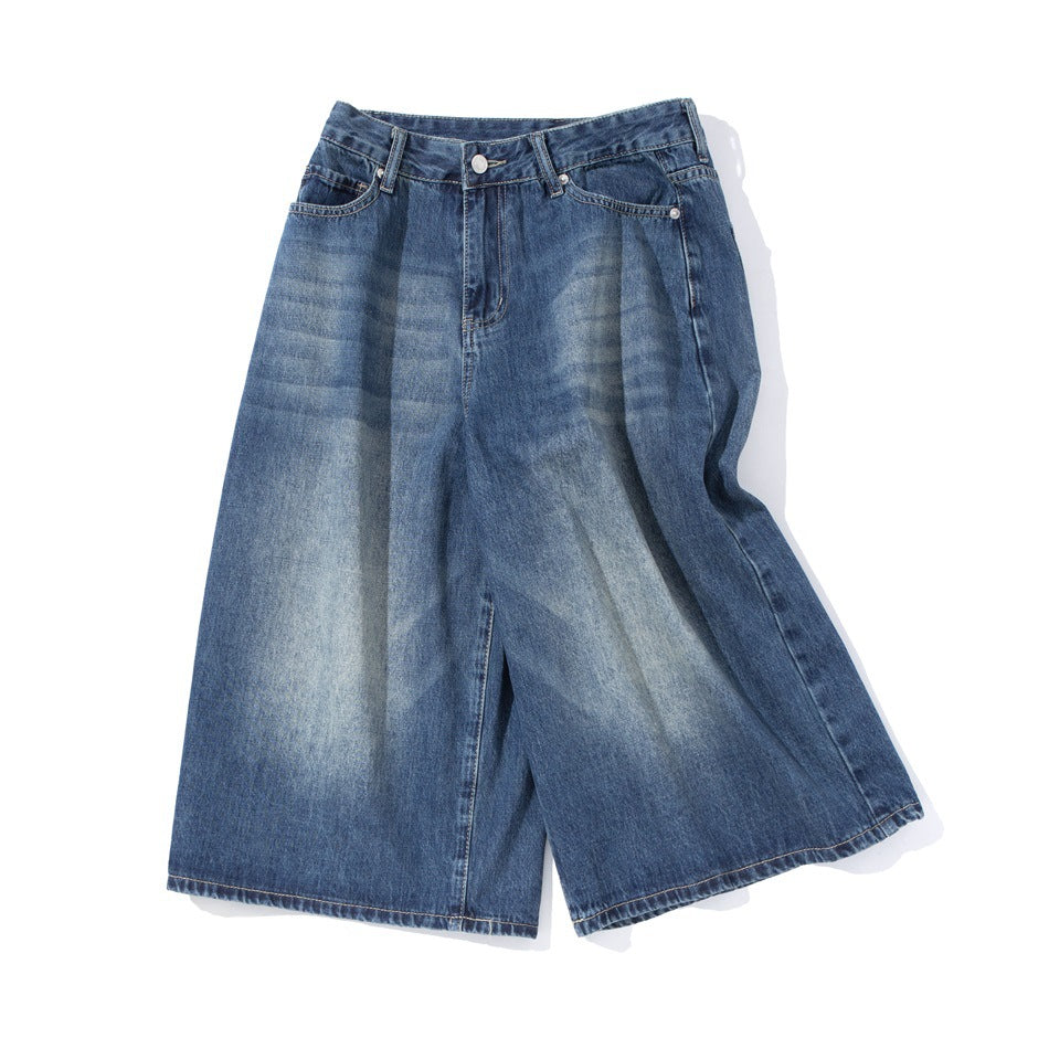Front view of dark blue wide-leg denim shorts with a button closure, belt loops, and faded patches.