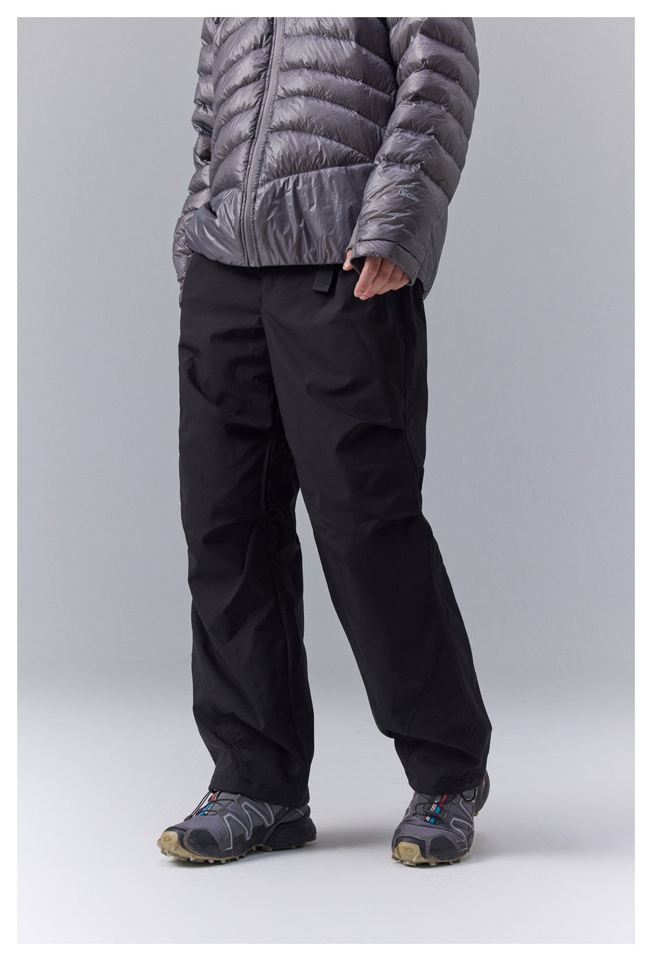 Angled view of a model wearing loose black pants with a metallic gray quilted jacket.