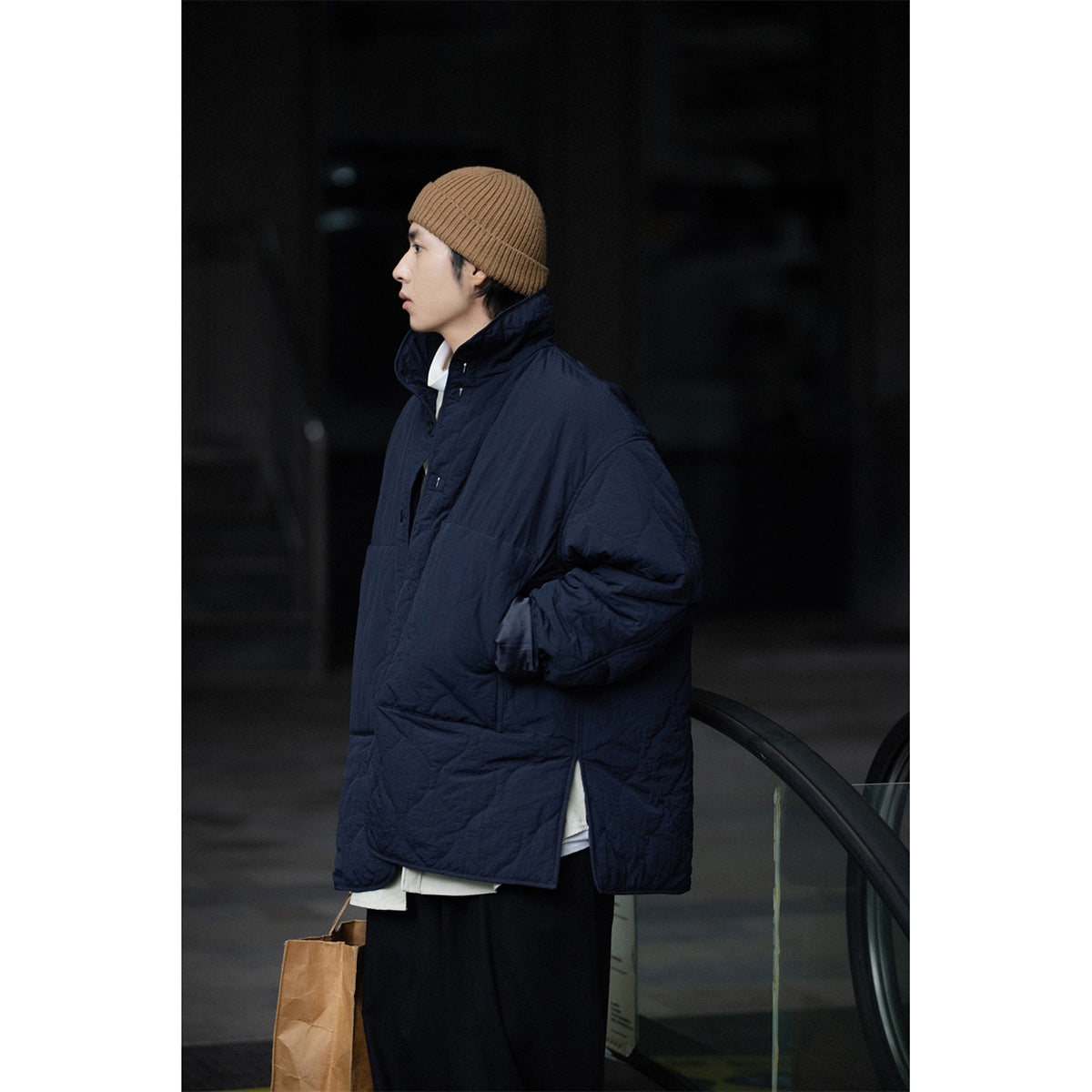 Side view of a model in a dark navy quilted coat with a raised collar and a brown knit beanie.