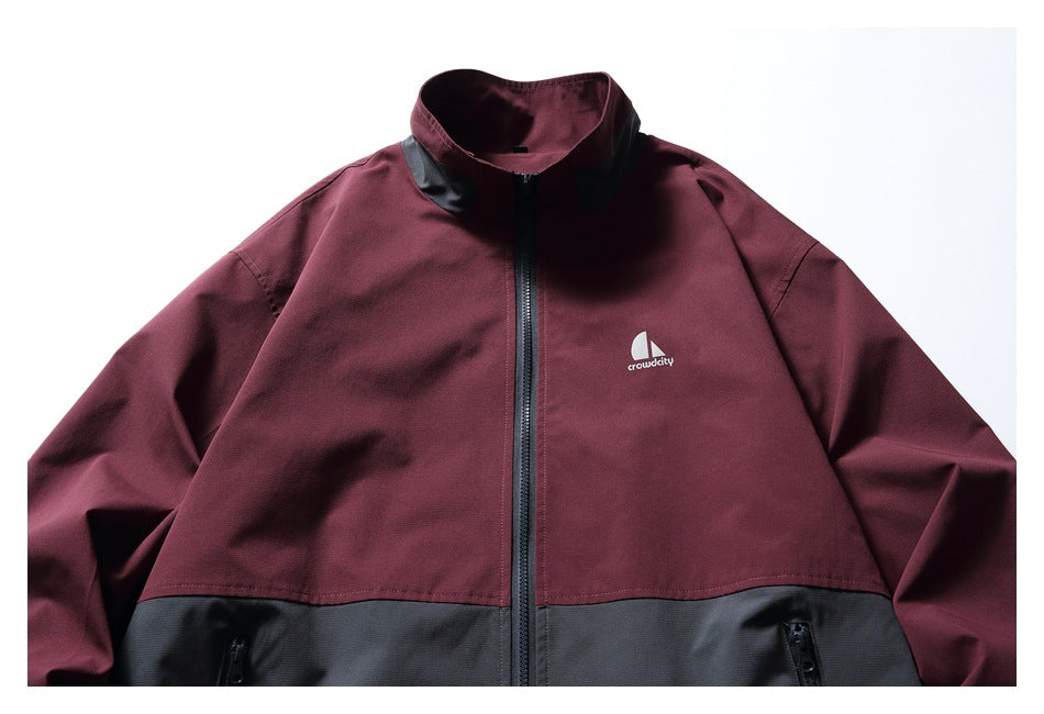 Front view of a burgundy and charcoal zip-up jacket with a high collar, black trim and white chest logo.