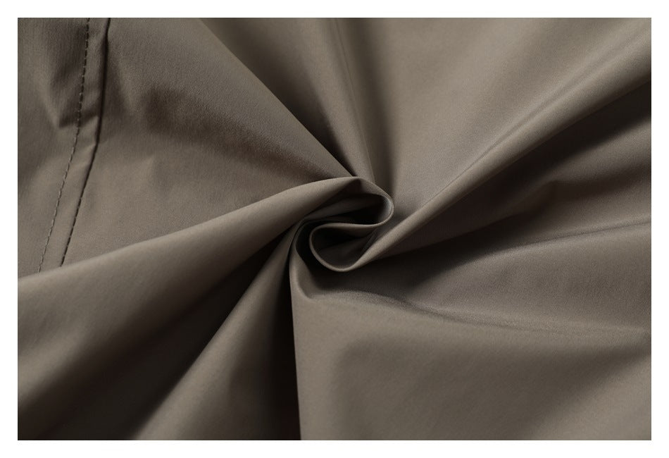 Close-up of smooth taupe-gray fabric gathered into folds, with a stitched seam along the left edge.
