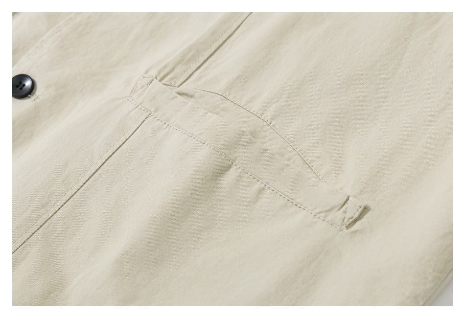 Close-up of a pale beige garment's welt pocket, stitching, and partial black button.