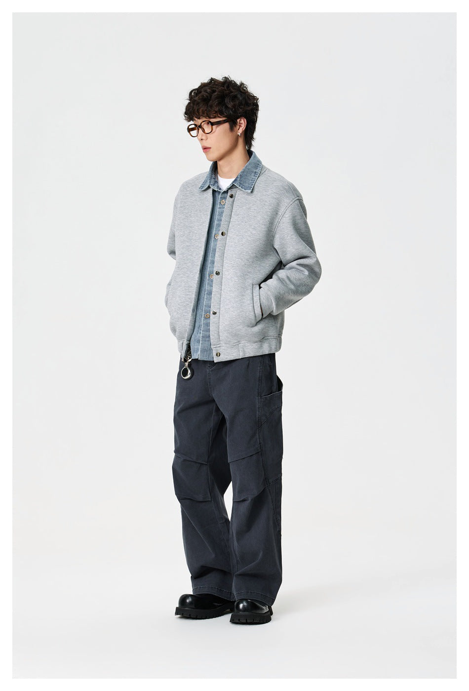 Three-quarter view of a model in a light gray denim-collar jacket, dark cargo pants and black shoes.