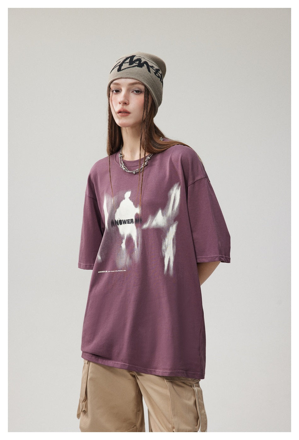 Model wearing an oversized plum graphic T-shirt with beige cargo pants and a taupe beanie.