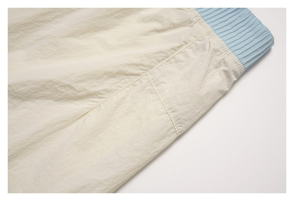 Close-up of cream garment fabric, stitched panel seams, and a pale blue ribbed elastic edge.