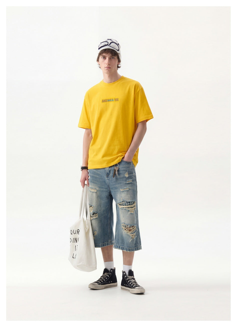 Man wearing yellow 'ANSWER ME' T-shirt with distressed denim shorts, beanie, tote bag and black high-top sneakers