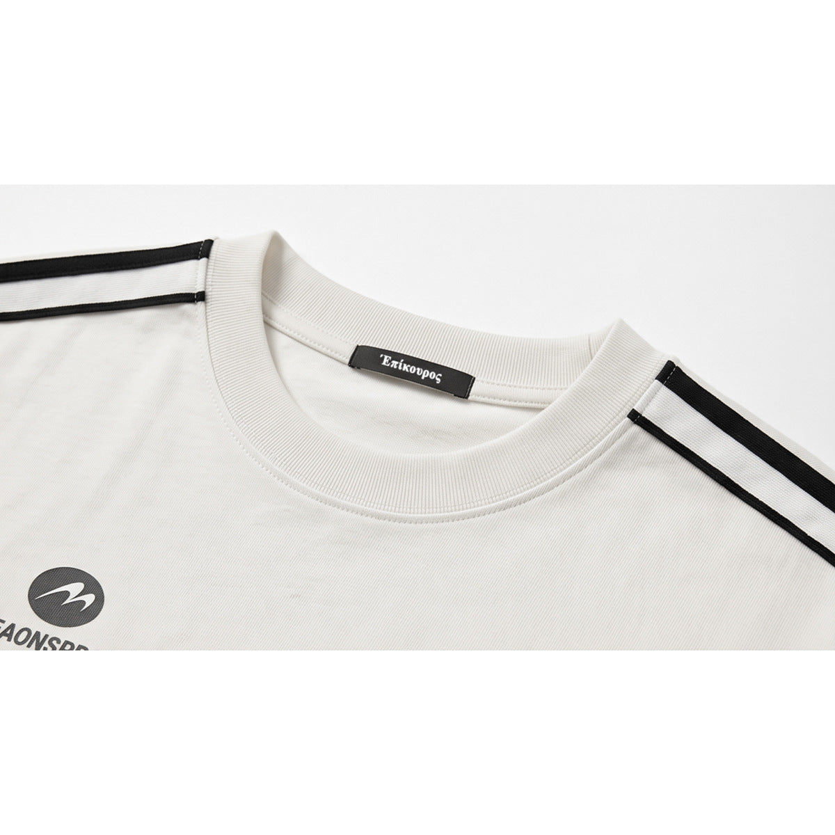 Close-up of a white crew-neck shirt with black shoulder stripes, a Greek-letter neck label, and part of a chest graphic.
