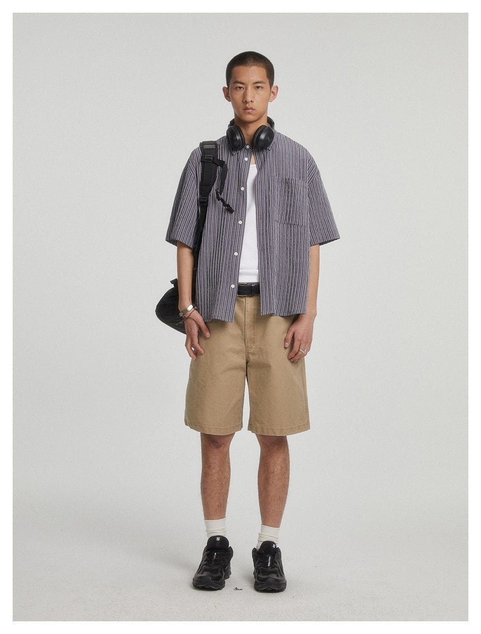 Model wearing khaki knee-length shorts with a striped short-sleeve shirt, white tank, black sneakers and a backpack