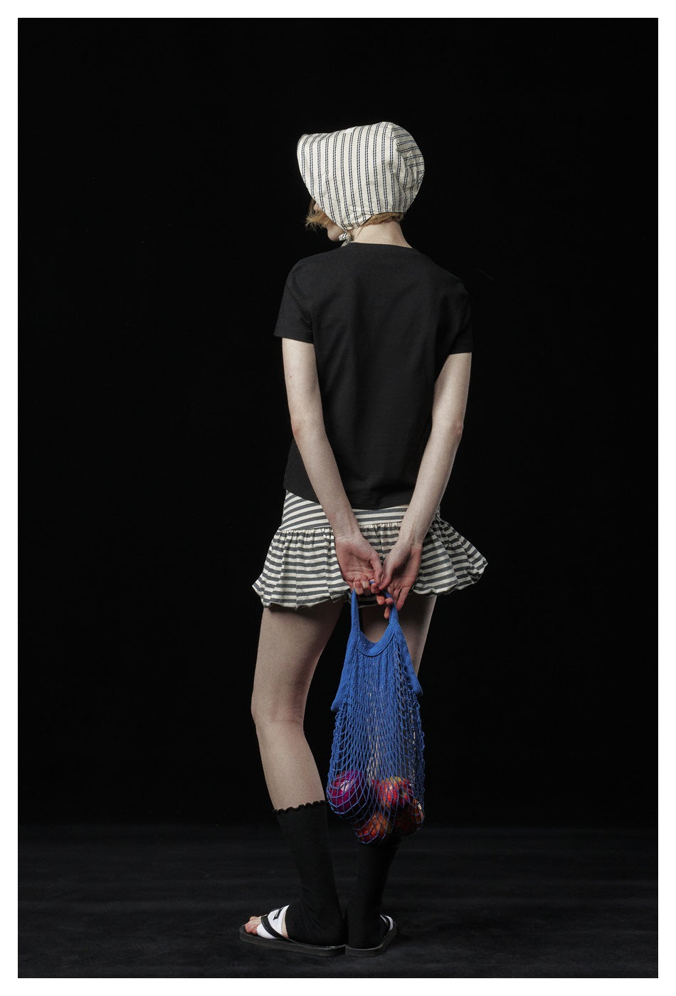 Rear view of a model wearing a plain black T-shirt and a gray-and-white striped ruffle skirt.