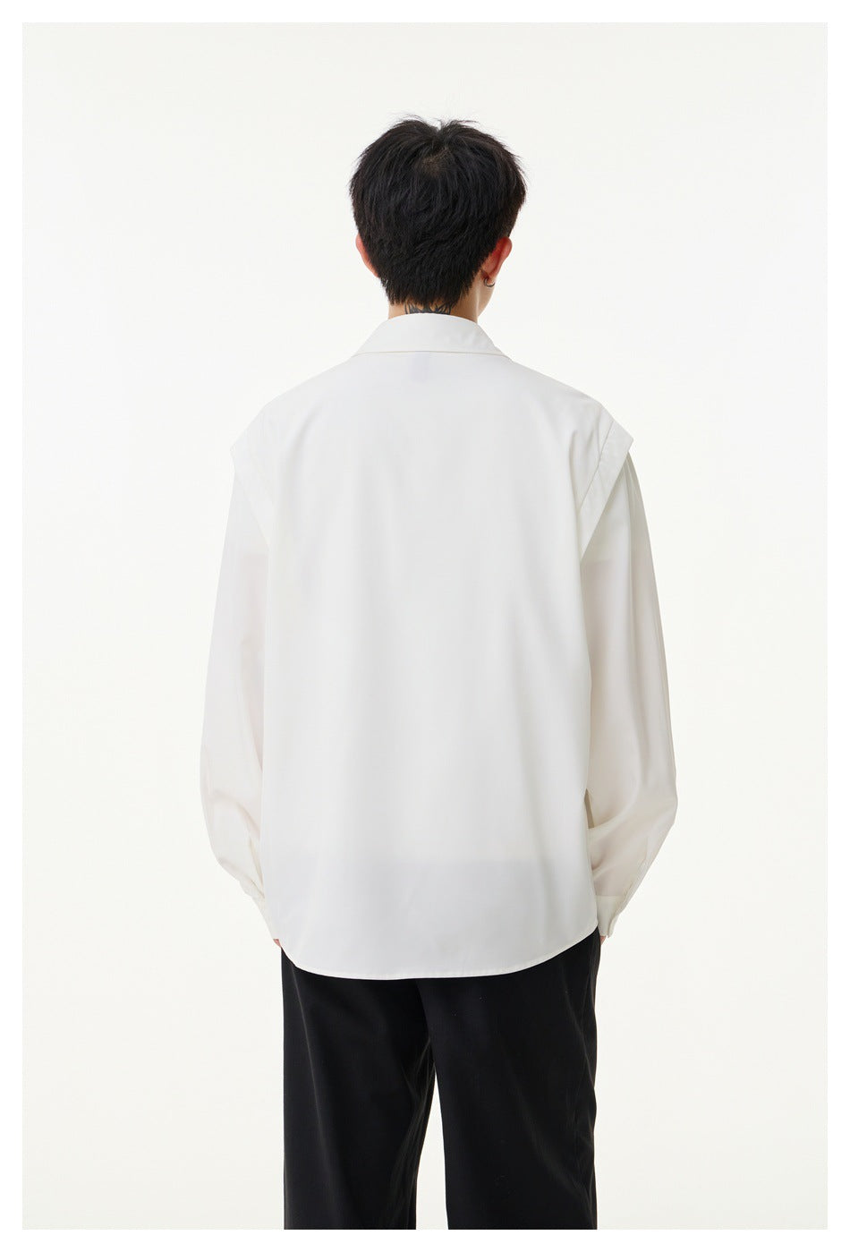 Back view of a model wearing a white long-sleeve button-up shirt with shoulder details and black trousers.