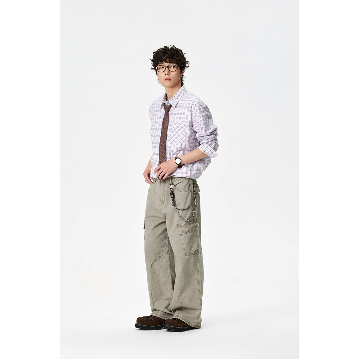 Model wearing a pale lavender plaid button-down shirt with a chest pocket and brown tie, paired with loose cargo pants.