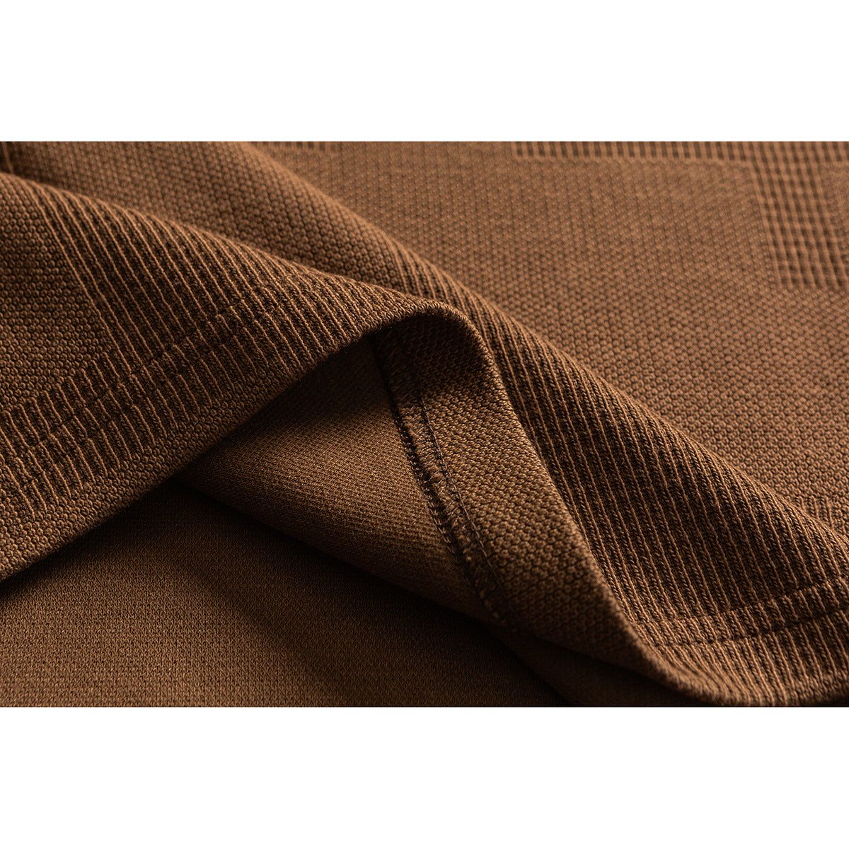 Close-up of camel-brown knit fabric folded to show its textured surface, ribbing, and seam.