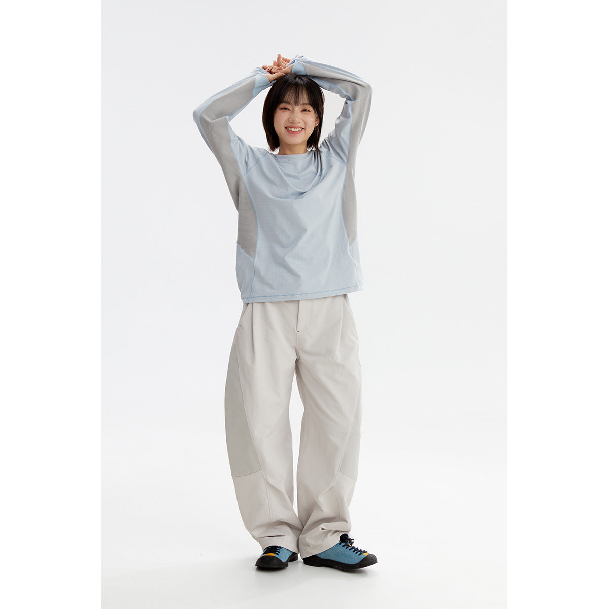 Model wearing a pale blue long-sleeve top with light gray panels and loose off-white trousers.