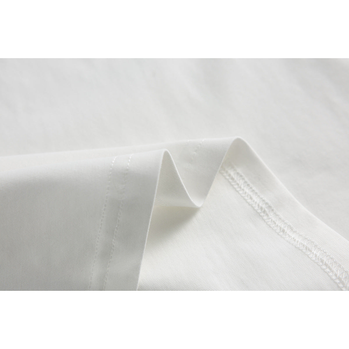 Close-up of white T-shirt fabric folded to show the seam and stitching.