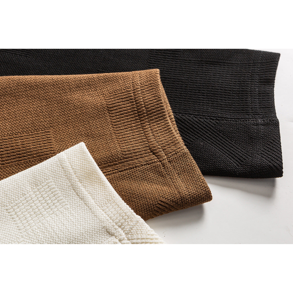 Close-up of folded ivory, camel-brown, and black knit garments showing textured fabric and ribbed edges.