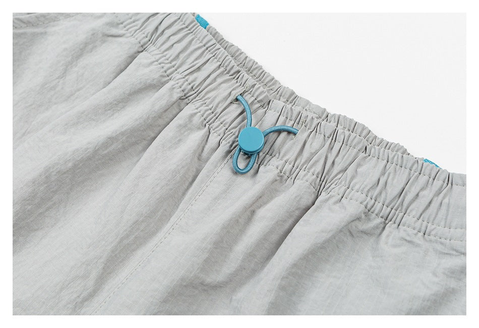 Close-up of light gray shorts with an elastic waistband and turquoise drawcord toggle.