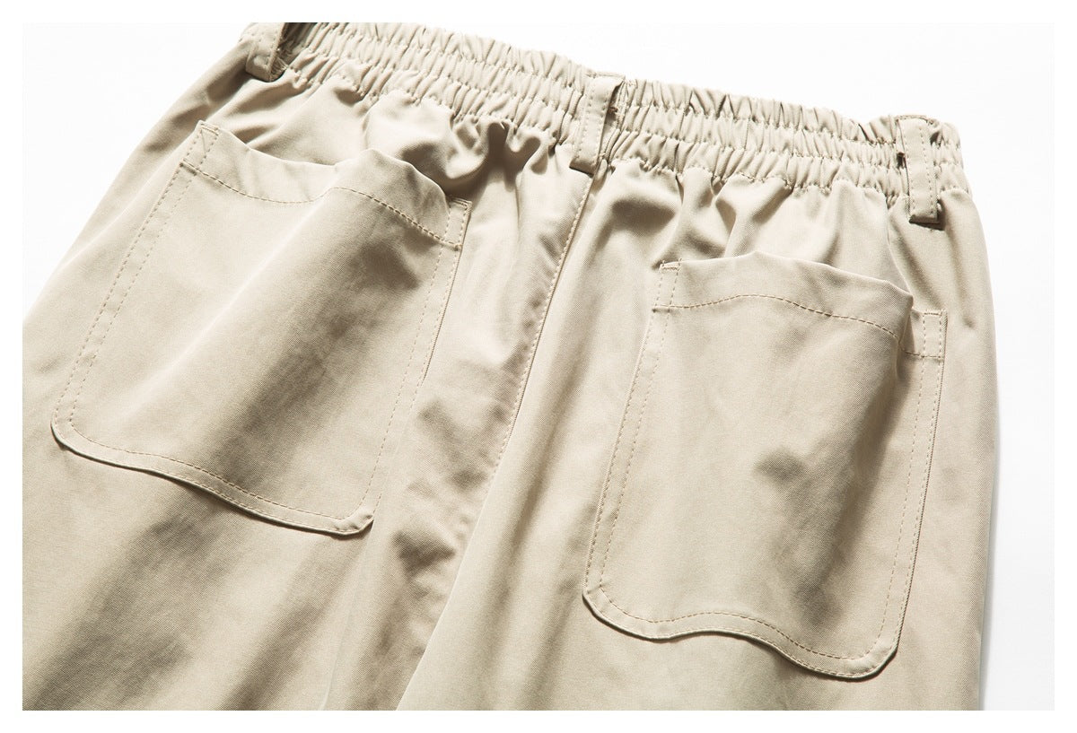 Close-up of beige pants showing an elastic waistband, belt loops, and two large patch pockets.
