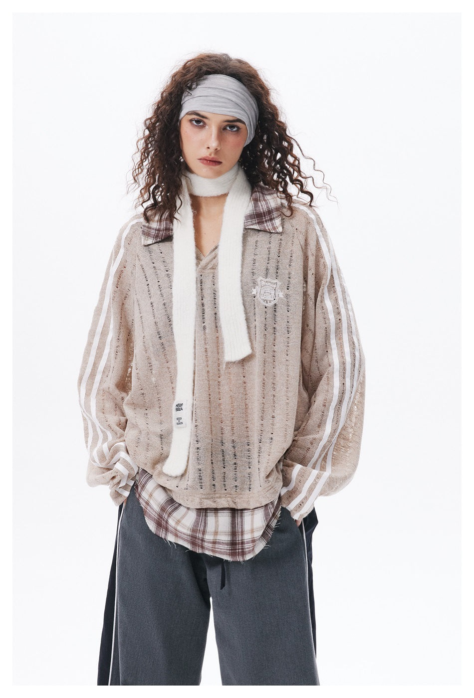 Model wearing a beige open-knit pullover with white sleeve stripes and plaid collar over a plaid shirt and dark wide-leg