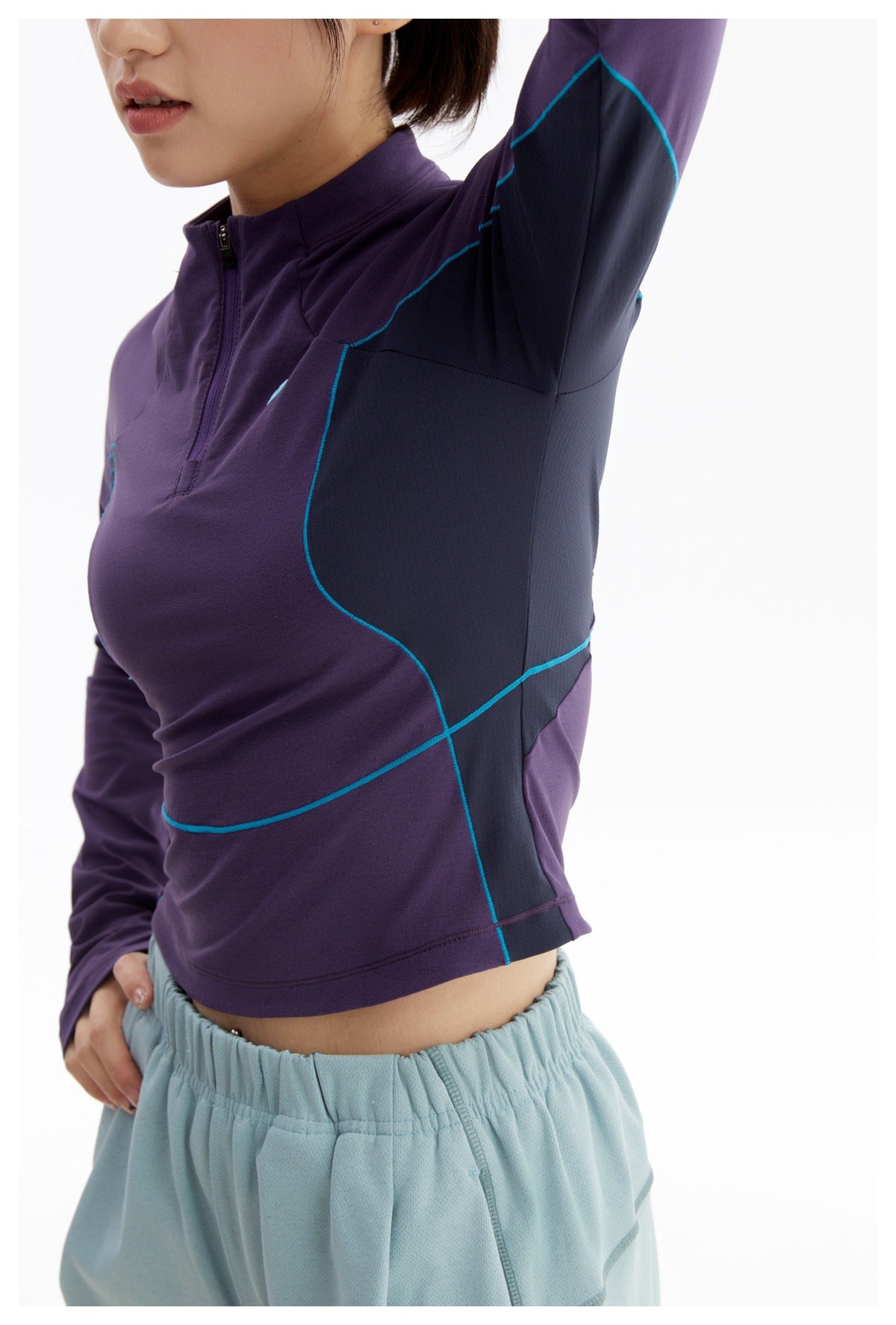 Close-up of a purple quarter-zip top showing its dark side panel, teal piping, and pale blue trouser waistband.