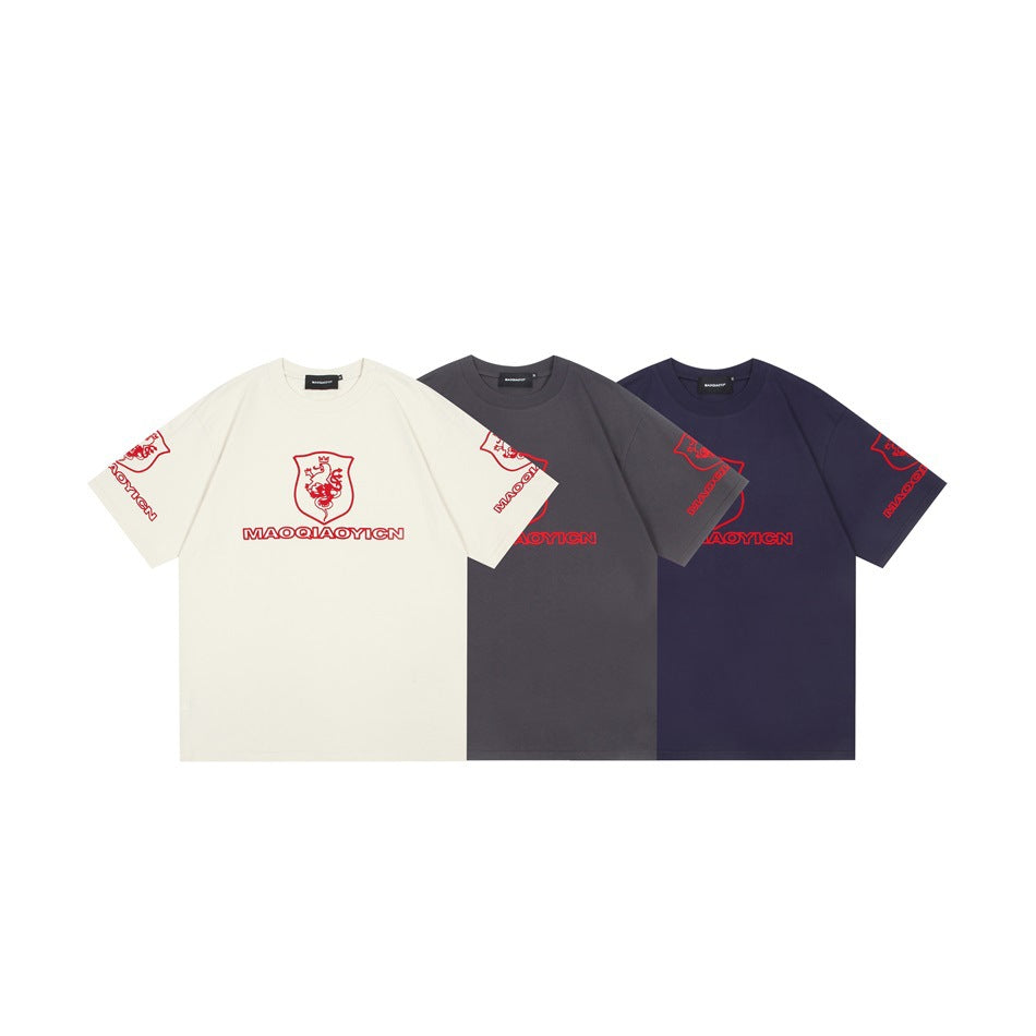 Front views of ivory, charcoal gray, and navy short-sleeve shirts with red shield graphics and sleeve prints.