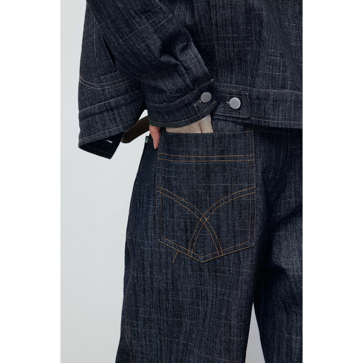 Close-up of a dark indigo jeans back pocket with curved orange stitching beneath a jacket cuff.