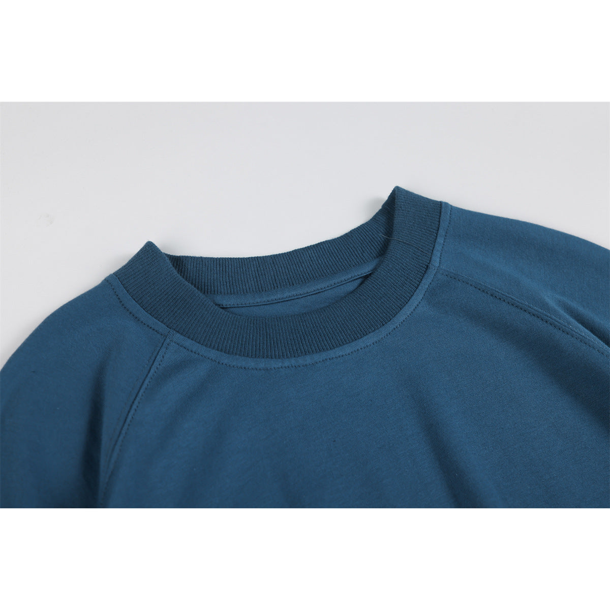 Close-up of a blue top showing its ribbed crew neckline and raglan shoulder seams.