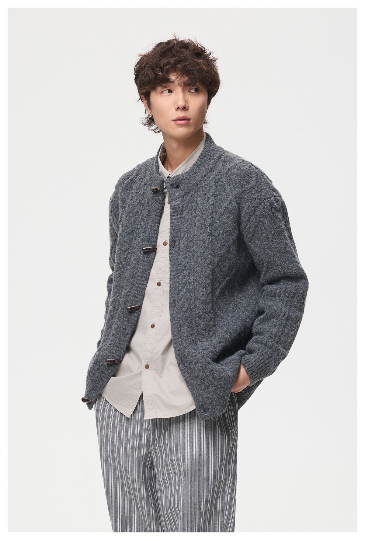 Model wearing a dark gray textured cardigan with toggle closures over a light shirt and striped trousers.