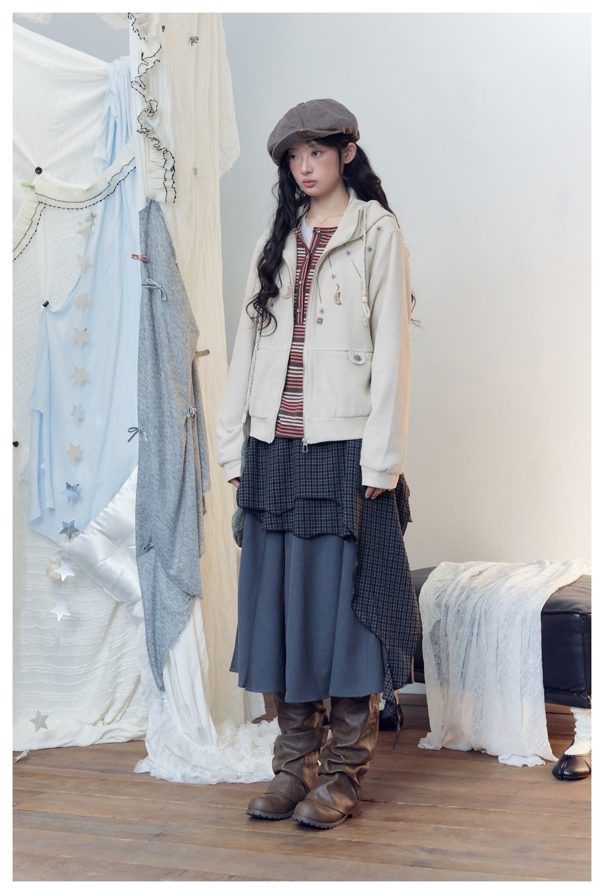 Model in a cream hooded zip jacket with moon buttons, turned slightly to the side, with a striped top and midi skirt