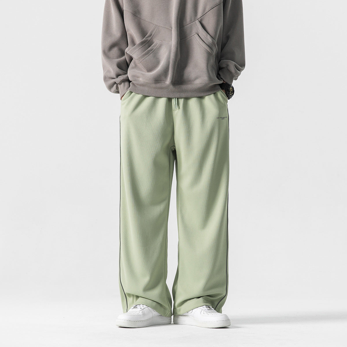 Front view of a model wearing pale sage wide-leg pants with a drawstring waist and dark piping.
