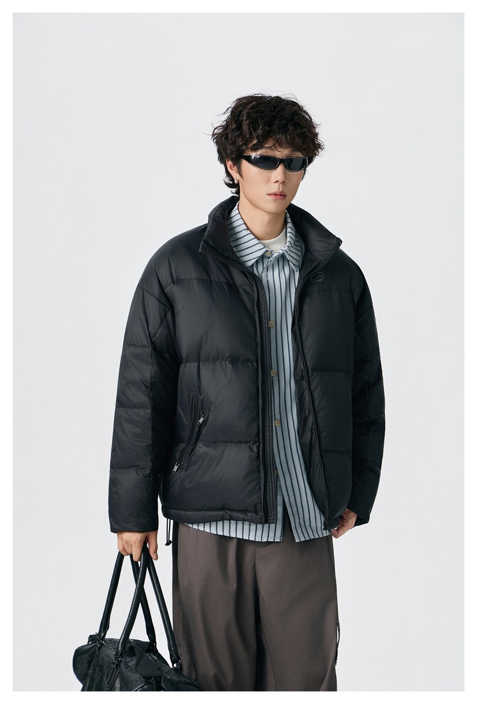 Front view of a model wearing an open black padded jacket over a striped shirt.