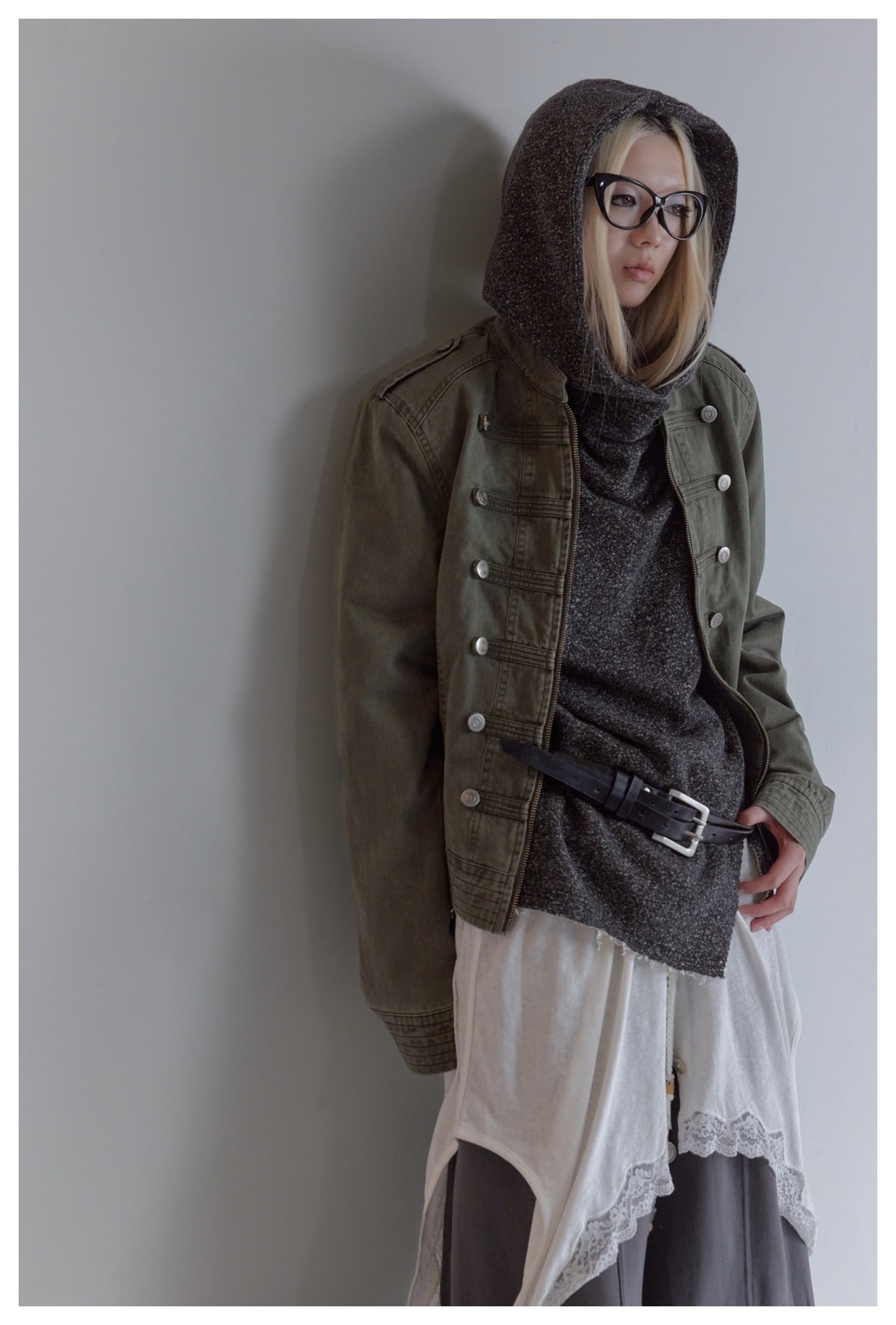 Closer view of a model wearing an olive jacket over a charcoal hooded top and white lace-trim layer.