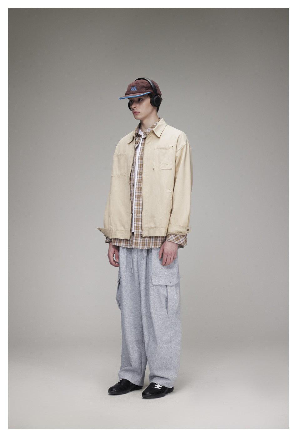 Model wearing a khaki zip jacket over a plaid shirt with gray cargo sweatpants, standing side-facing